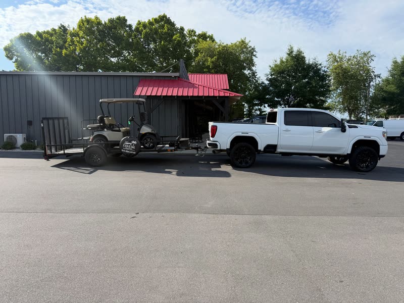 Golf cart loaded on a trailer behind a pickup, ready for delivery